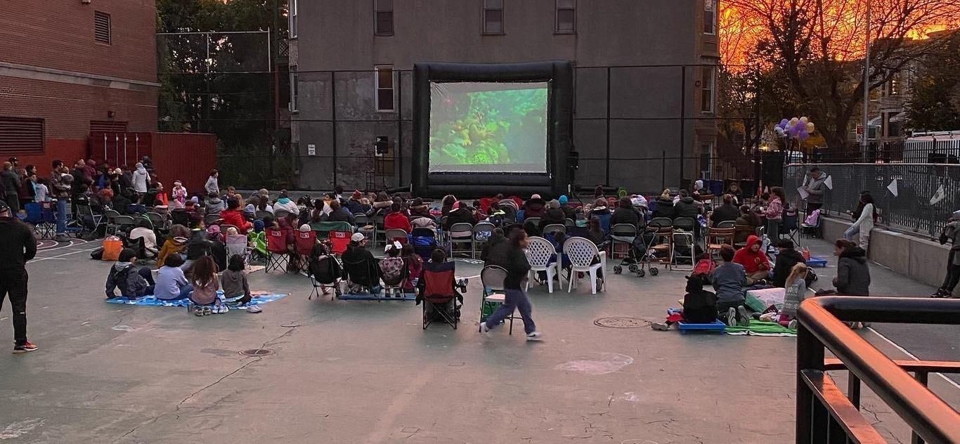 Families watching a movie on a big screen in the schoolyard at sunset